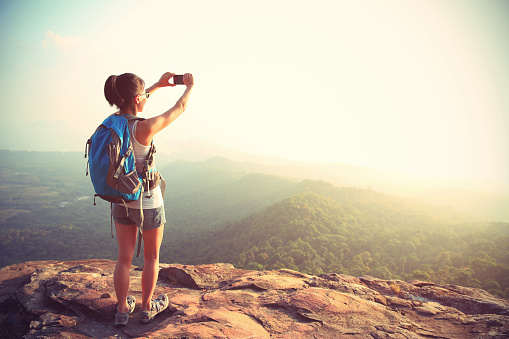 young woman hiker taking photo with smart phone at mountain peak