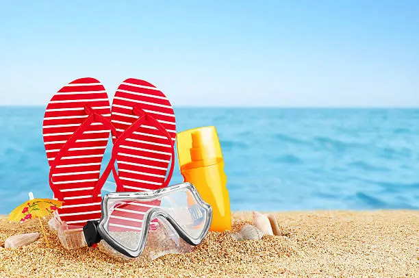 Photo of Flip-flops, sunscreen spray and diving masks on the beach.