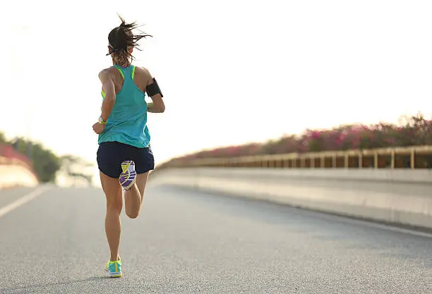 Photo of young woman runner running on city bridge road