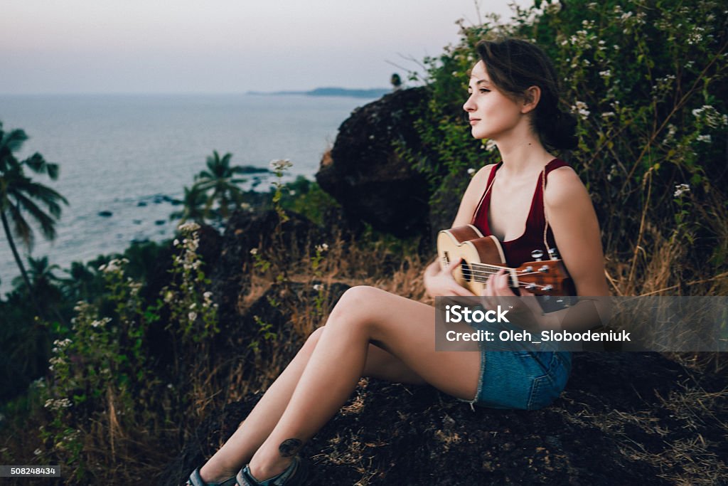 Woman with ukulele Woman sitting with ukulele on the background of sea and palm trees India Stock Photo