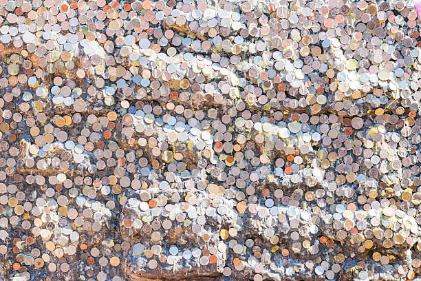 Close-up of a log covered with coins and topped with a brick holding coins. Blurred grass in background.