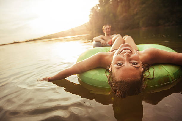 Young girl in lake on innertube Portrait of happy young woman floating in an innertube with her boyfriend in background at the lake. Young couple in lake on inflatable rings. inner tube stock pictures, royalty-free photos & images