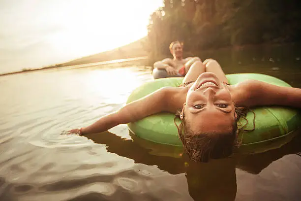 Portrait of happy young woman floating in an innertube with her boyfriend in background at the lake. Young couple in lake on inflatable rings.