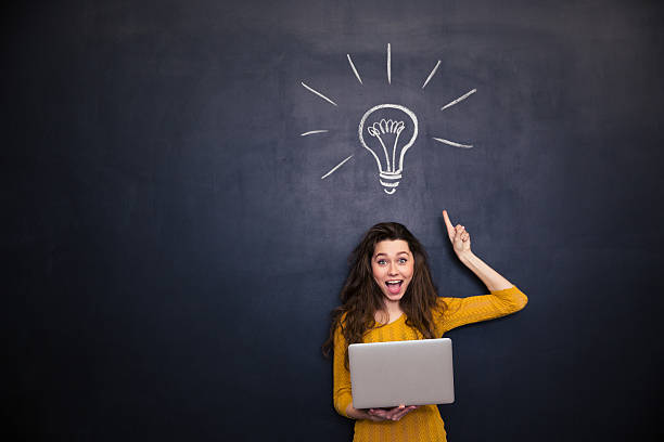 feliz mulher segurando computador portátil e ter idéia sobre fundo de quadro-negro - inventor - fotografias e filmes do acervo