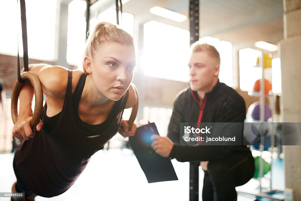 Woman with her personal trainer exercising on gymnastic rings Fit young woman with her personal fitness trainer in the gym exercising with gymnastic rings Fitness Instructor Stock Photo