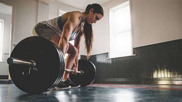 Preparing for a Deadlift Muscular professional female powerlifter doing a deadlift in an empty gym space, copy space is on the right side of the image. Uploaded as part of the Lean In Collection. deadlift stock pictures, royalty-free photos & images