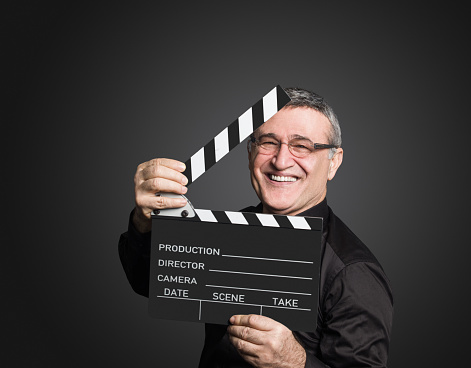 Senior movie director holding a movie clapper over isolated gray background, studio shot. Image taken with Hasselblad H5D 50C camera system and developed from camera RAW.