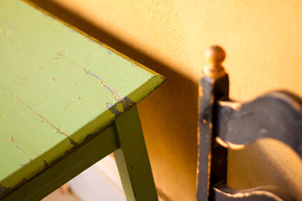 Detail from a rustic kitchen: a chipped green table, old black chair, and a rough yellow adobe wall. Shot in Santa Fe, New Mexico.