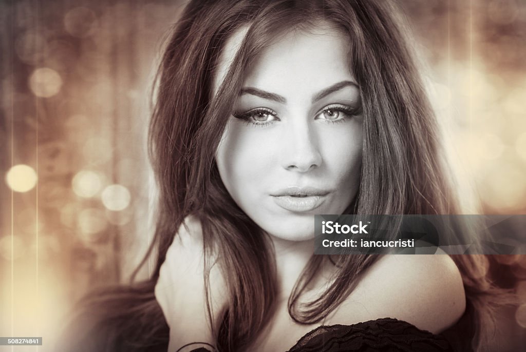 Genuine natural brunette looking directly to the camera Beautiful female portrait with long hair, studio shot. Genuine natural brunette looking directly to the camera. Attractive woman with beautiful eyes with lights in background, black and white photo Adult Stock Photo