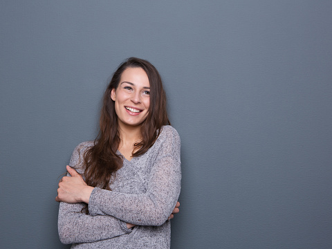 Close up portrait of a young woman laughing with arms crossed on gray background