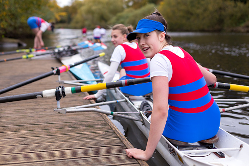 A group of teenage girls are training for their rowing team on the river. They can be seen pushing off from the pier.