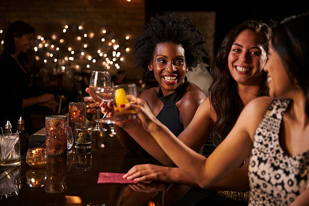 Female Friends Enjoying Night Out At Cocktail Bar Female Friends Enjoying Night Out At Cocktail Bar black people bar stock pictures, royalty-free photos & images