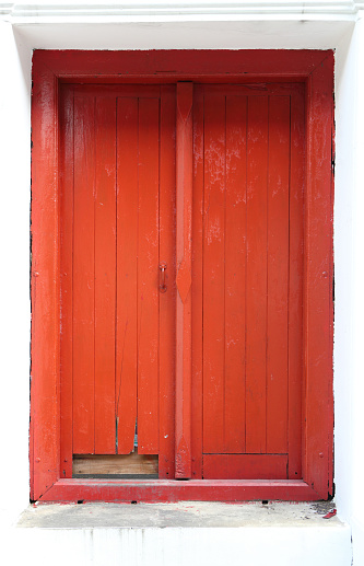 Red railings lead up a set of front stairs to a open red door with an arched window above.