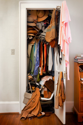 Messy closet in bedroom overstuffed with clothes, hats, woman's apparel.