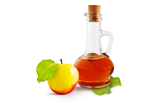Apple cider vinegar cruet and ripe apples with green leaves on a white background