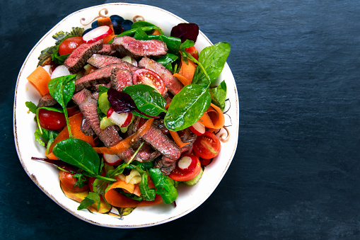 Spicy Beef Meat Salad with Carrots, Tomatoes, Cucumber, Parsley and Salad leaves Spinach, rocket, red ruby chard on blue stone background.