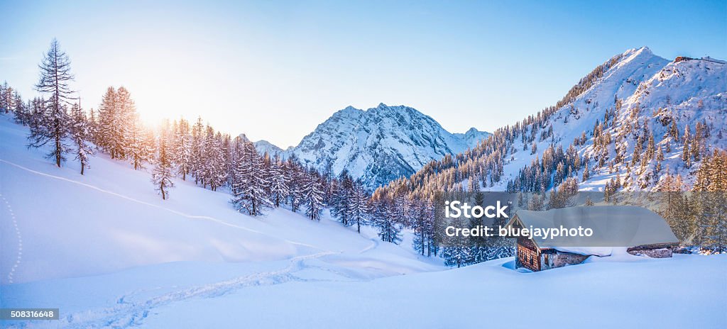Winter wonderland in the Alps with mountain chalet at sunset Panoramic view of beautiful winter wonderland mountain scenery with traditional mountain cabin the background in the Alps in golden evening light at sunset. Snow Stock Photo
