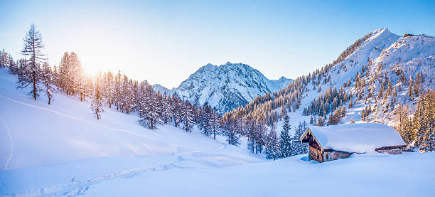 Winter wonderland in the Alps with mountain chalet at sunset Panoramic view of beautiful winter wonderland mountain scenery with traditional mountain cabin the background in the Alps in golden evening light at sunset. hut stock pictures, royalty-free photos & images