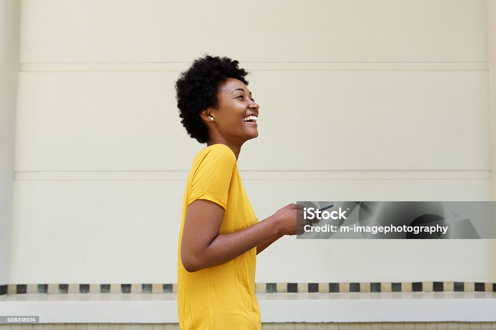 Cheerful young african woman walking with a mobile phone Side portrait of cheerful young african woman walking with a mobile phone Women Stock Photo