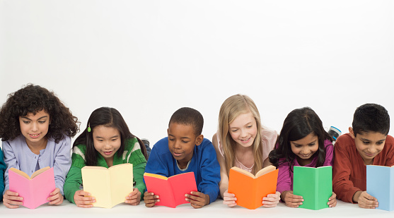 A multi-ethnic group of elementary age students are lying together in a row and are reading books.