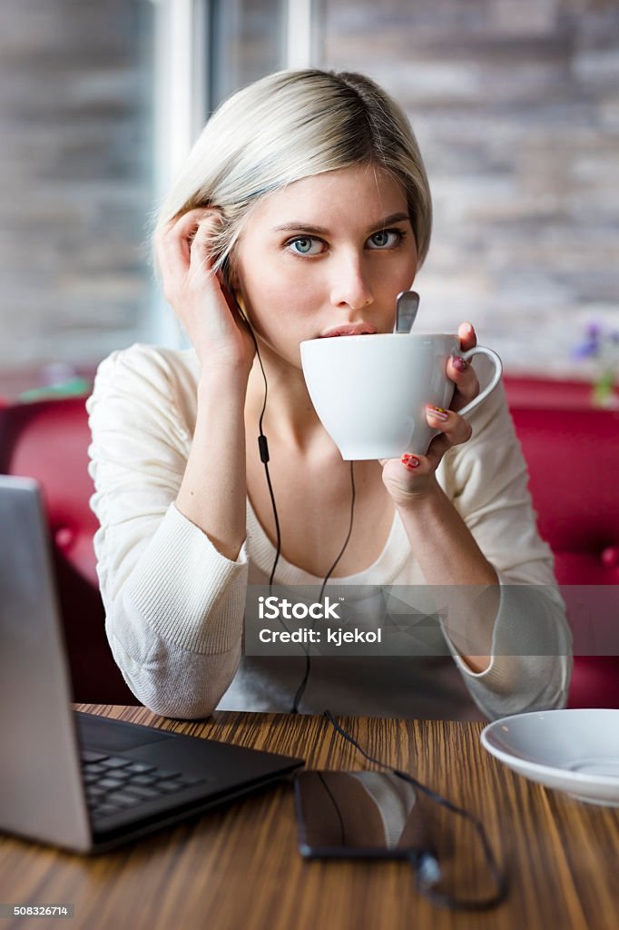 Woman working with laptop computer in cafe Focused woman with laptop and smart phone drinking coffee and doing business or study in a cafe. Looking into camera. Adult Stock Photo