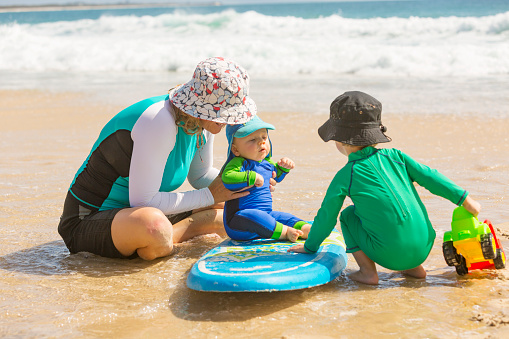 Mother and young children wearing sun protection clothing at the beach