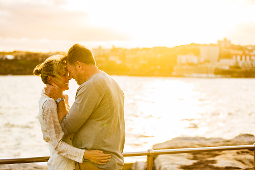 Happy and healthy middle aged active and fit couple sharing a hug outdoor by the seaside at Bondi Beach in Sydney, Australia at sunset