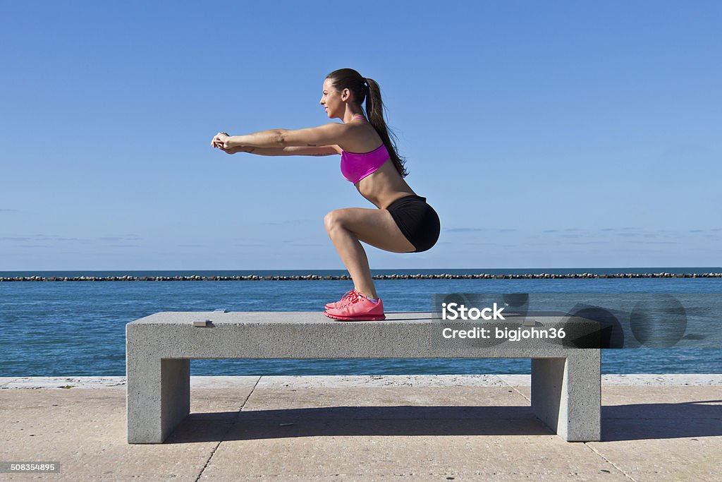 Hispanic woman doing squats by the water Hispanic woman doing squats on a bench by the ocean Adult Stock Photo