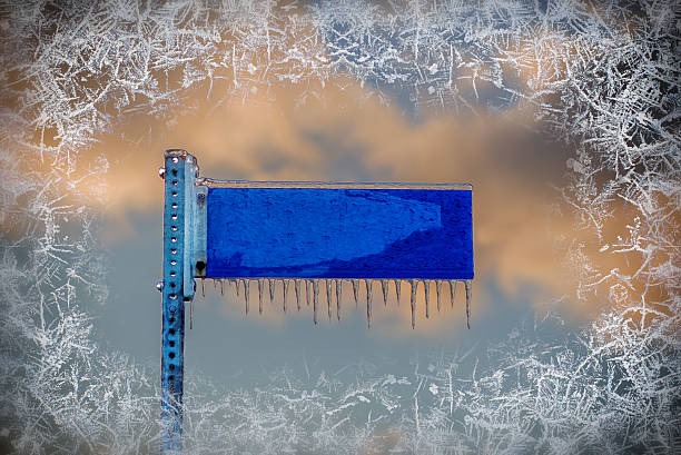A close up of a frozen blank blue street sign covered in ice and icicles with a frost border surrounding the image.  Room for Copy Space.