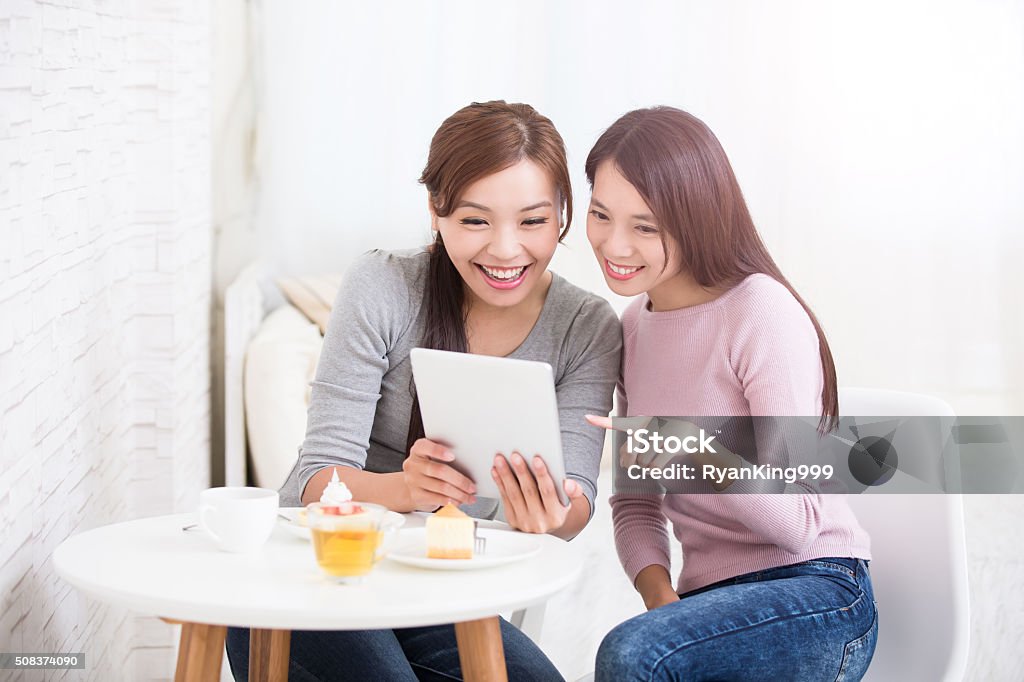 happy young female friends Two happy young female friends use digital tablet pc with tea, coffee and cakes, healthy lifestyle and tecnology concept, asian beauty Adult Stock Photo