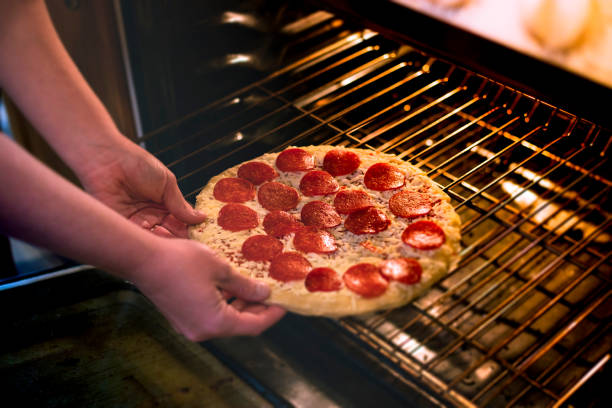 A stock photograph of a womans hands placing a store bought frozen pizza into the oven. Photographed with the Canon EOS 5DSR at 50mp