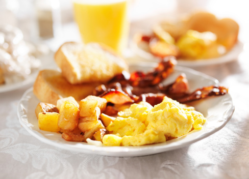 full breakfast with scrambled eggs, fried potatoes and bacon, shot close up with selective focus on white table cloth