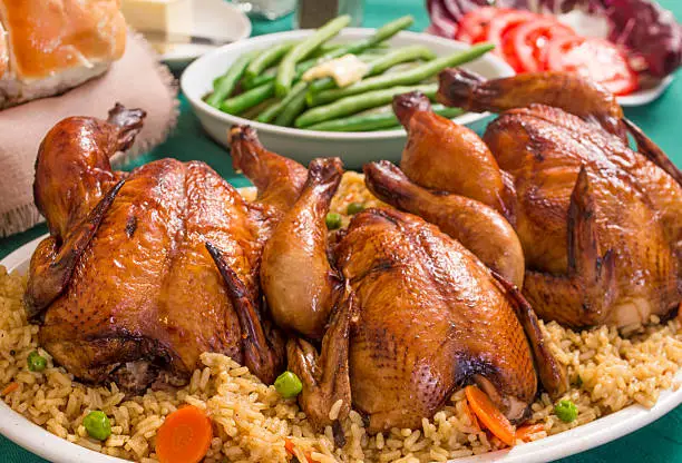 holiday dinner with cornish game hens on a bed of rice served with rolls salad and fresh green beans