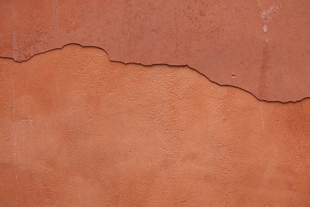 Old terracotta painted stucco wall with cracked plaster. Background texture.