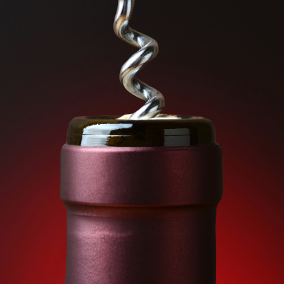 Closeup of the neck of a wine bottle with a corkscrew partially in the cork.  Over a light to dark red background in square format.