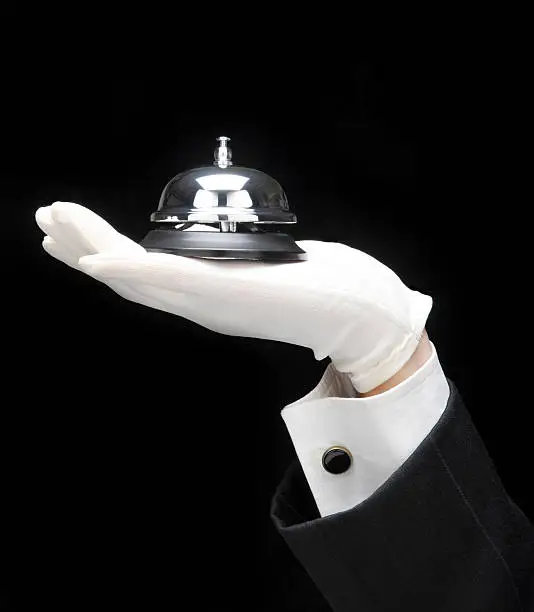Butlers outstretched hand and arm with service bell, over a black background