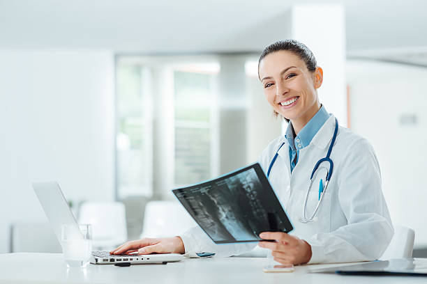 sorridente feminino médico examinando uma radiografia - radiologist imagens e fotografias de stock