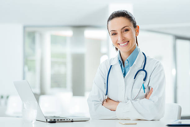 Confident female doctor at office desk Confident female doctor sitting at office desk and smiling at camera, health care and prevention concept female doctor stock pictures, royalty-free photos & images