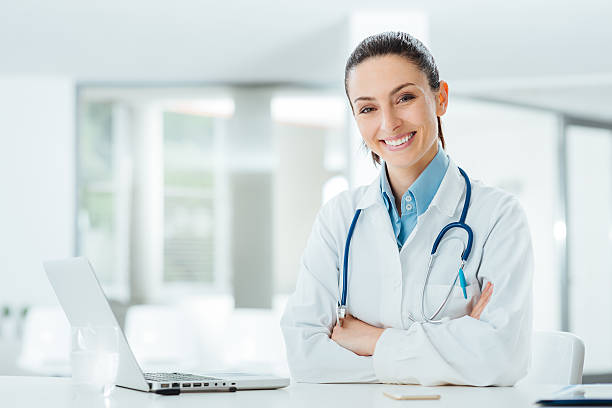 Confident female doctor at office desk Confident female doctor sitting at office desk and smiling at camera, health care and prevention concept beauty clinic stock pictures, royalty-free photos & images