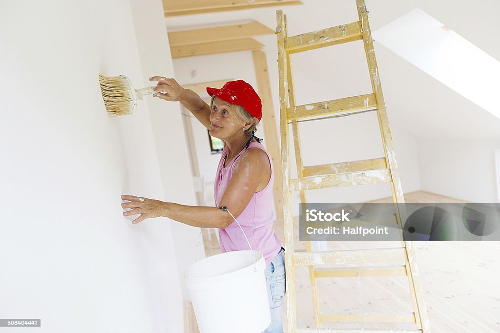 Senior woman painting Senior woman painting wall in new house. She is using ladder. Active Lifestyle Stock Photo