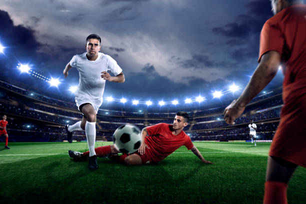 Professional soccer player dribbles ball on football pitch in outdoor floodlit stadium full of spectators under stormy evening sky