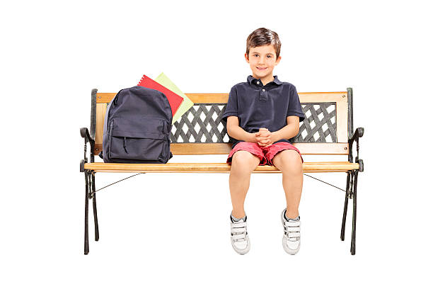 Little schoolboy sitting on a bench with backpack Little schoolboy sitting on a bench with a backpack isolated on white background sitting on bench stock pictures, royalty-free photos & images