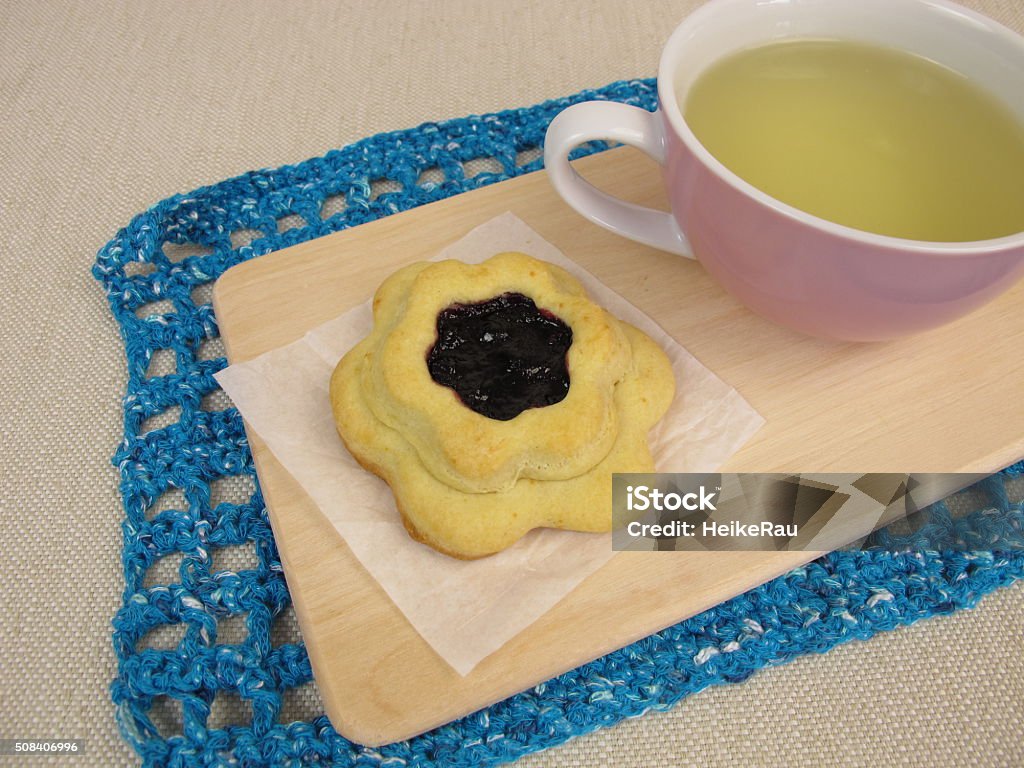Tea and flower biscuit filled with blueberry jam Tea and flower biscuit filled with blueberry jam - Mit Blaubeermarmelade gefüllter Blümchenkeks und Tee Afternoon Tea Stock Photo