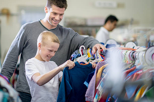 Father and Son Shopping Together A little boy and his father are looking through a rack of clothes while shopping together. The boy has pulled out a long sleeve shirt to buy. discount store stock pictures, royalty-free photos & images