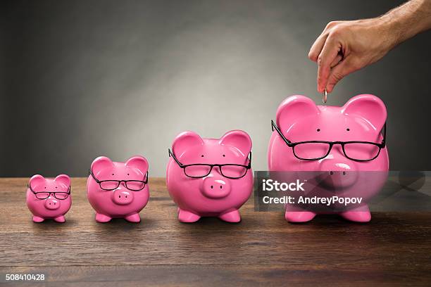 Foto de Pessoa Mão Ao Inserir Moeda Em Piggybank e mais fotos de stock de Poupança - Poupança, Cofre de porquinho, Grande