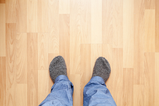 Male feet in blue pants and gray woolen socks stand on wooden floor