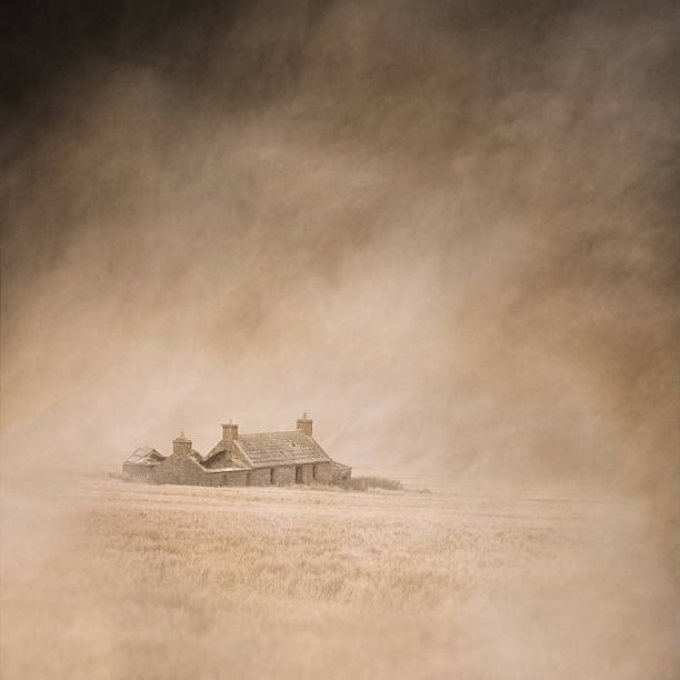 Derelict farm cottage in a vast, dusty, windswept cornfield captured using long exposure, bokeh and other effects with some areas blurred to create a surreal and dreamlike effect.