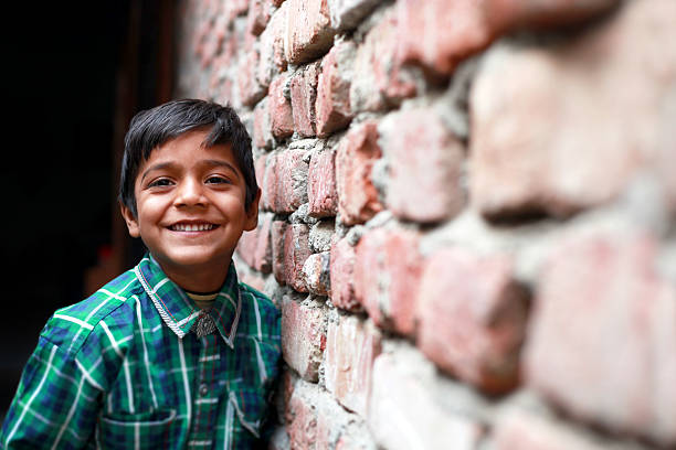 Little Boy Standing Portrait Cheerful little poor boy standing portrait near brick wall at his home and looking to the camera portrait close up.  developing countries photos stock pictures, royalty-free photos & images