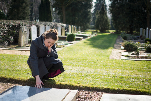 Woman sitting at grave with hand on grave