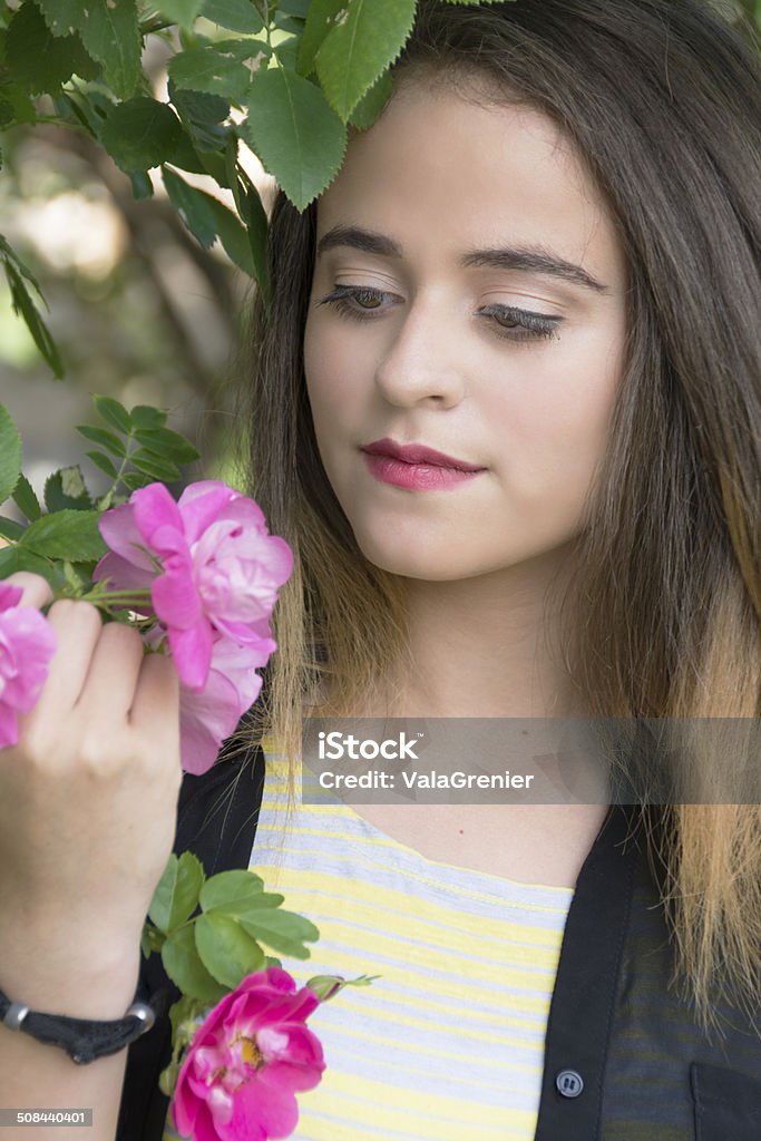 Serious 15 year old in rose garden. Vertical outdoor garden shot of 15 year old in summer clothes looking at pink climbing roses. Black Color Stock Photo